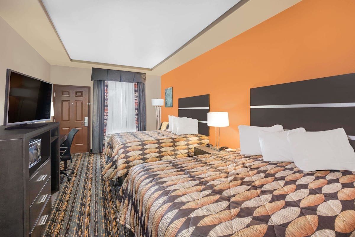 A hotel room with two beds, a TV, a desk, and a window with curtains.
