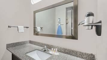 A bathroom with a granite countertop, a sink, a mirror, a towel rack, and a hairdryer mounted on the wall.
