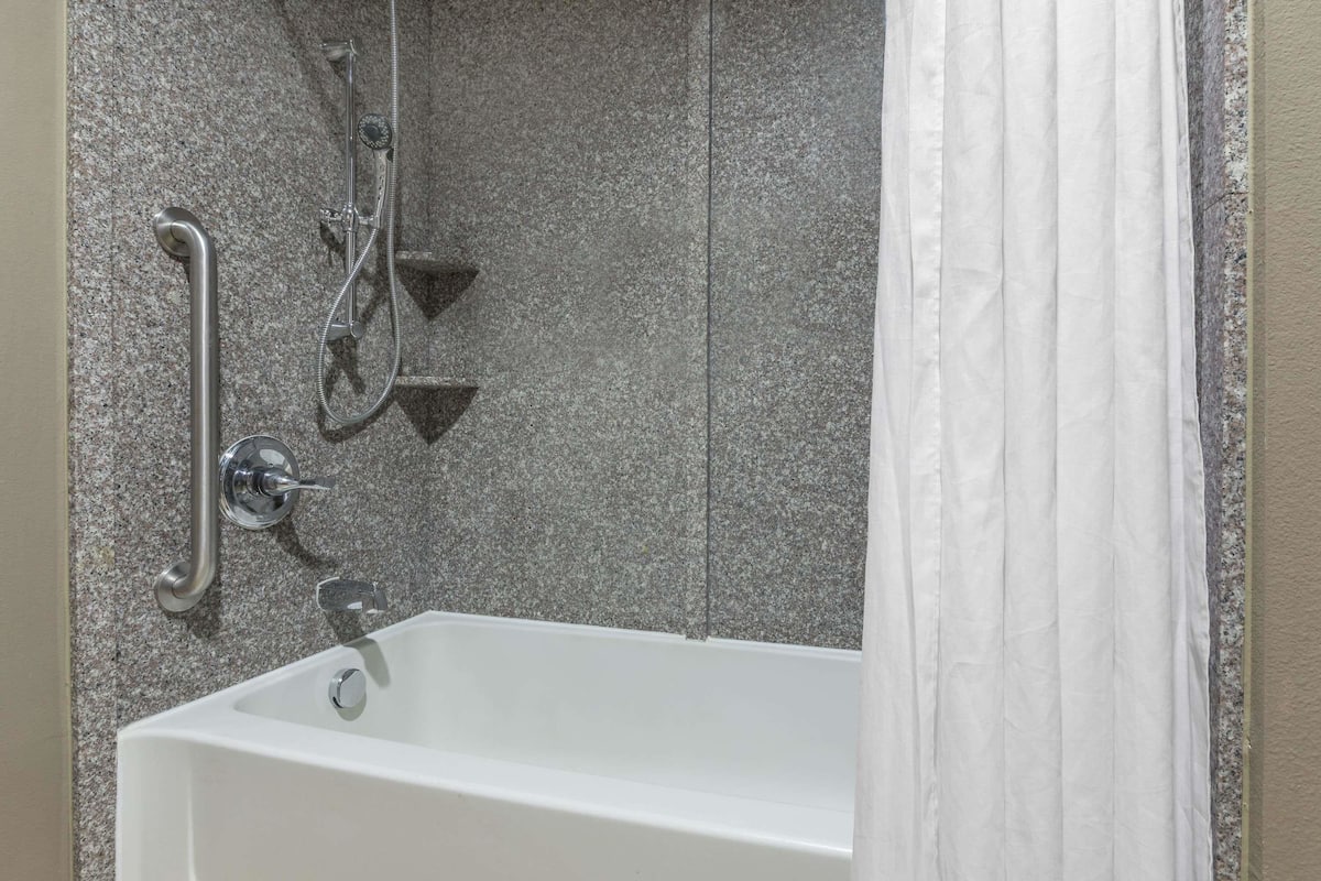 A bathroom with a white bathtub, a shower with a handheld showerhead, and a grab bar.