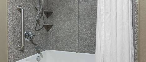 Un baño con una bañera blanca, una ducha con cabezal de ducha de mano y un pasamanos.