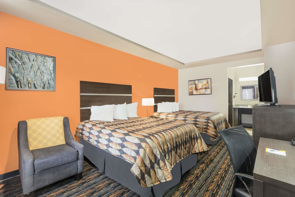 A hotel room with two beds, a desk, a chair, and a television.