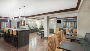 A modern hotel lobby with a central bar area, seating arrangements, and a kitchen in the background. - Days Inn by Wyndham Dilley (Dilley)