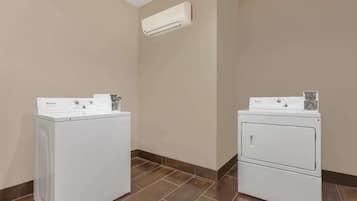 A laundry room with two Whirlpool washers and dryers, beige walls, and a tiled floor.