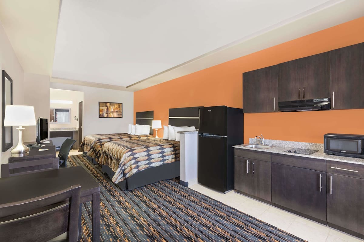 A hotel room with a bed, desk, chair, and kitchenette.