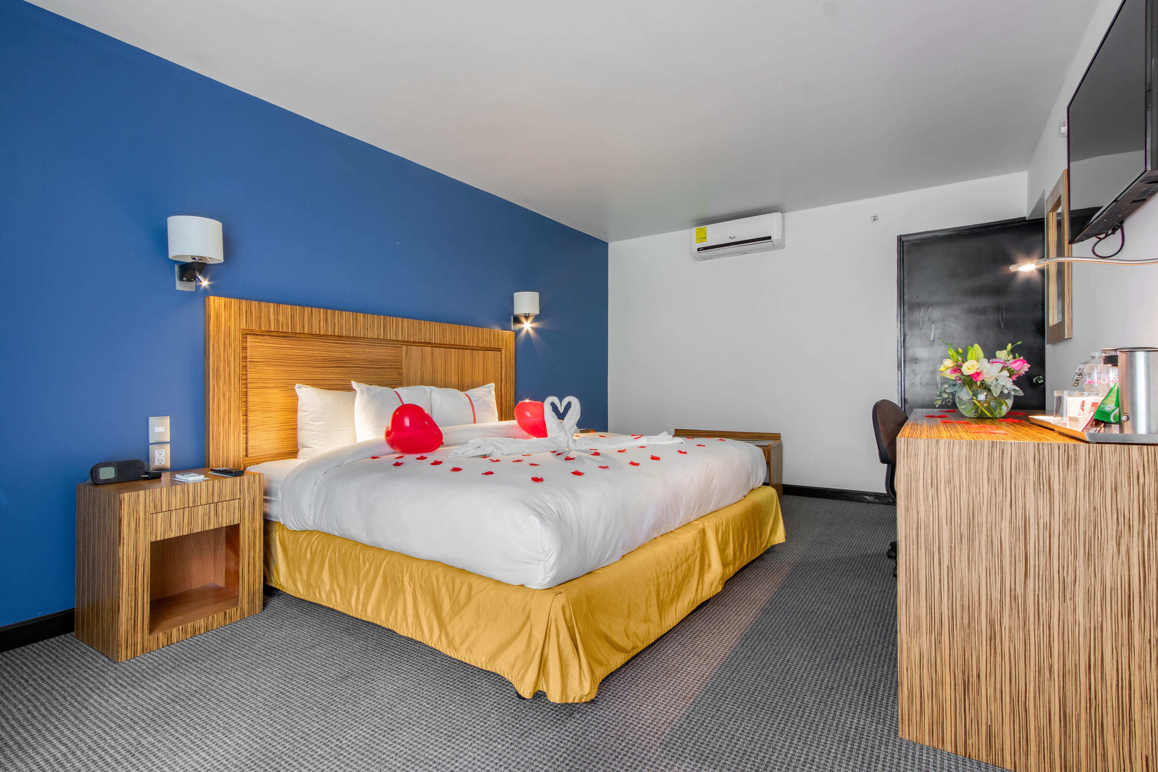 Habitación de hotel con una cama grande, cabecera de madera, mesitas de noche, un escritorio y un espejo.