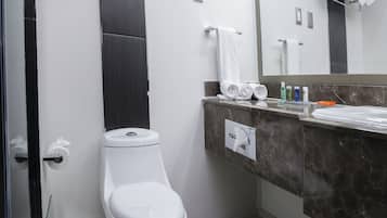 Un baño moderno con inodoro, lavamanos con encimera de mármol y espejo.