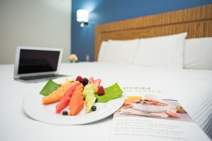 A hotel room with a bed, a laptop on the bed, a fruit plate, and a brochure on the bed.