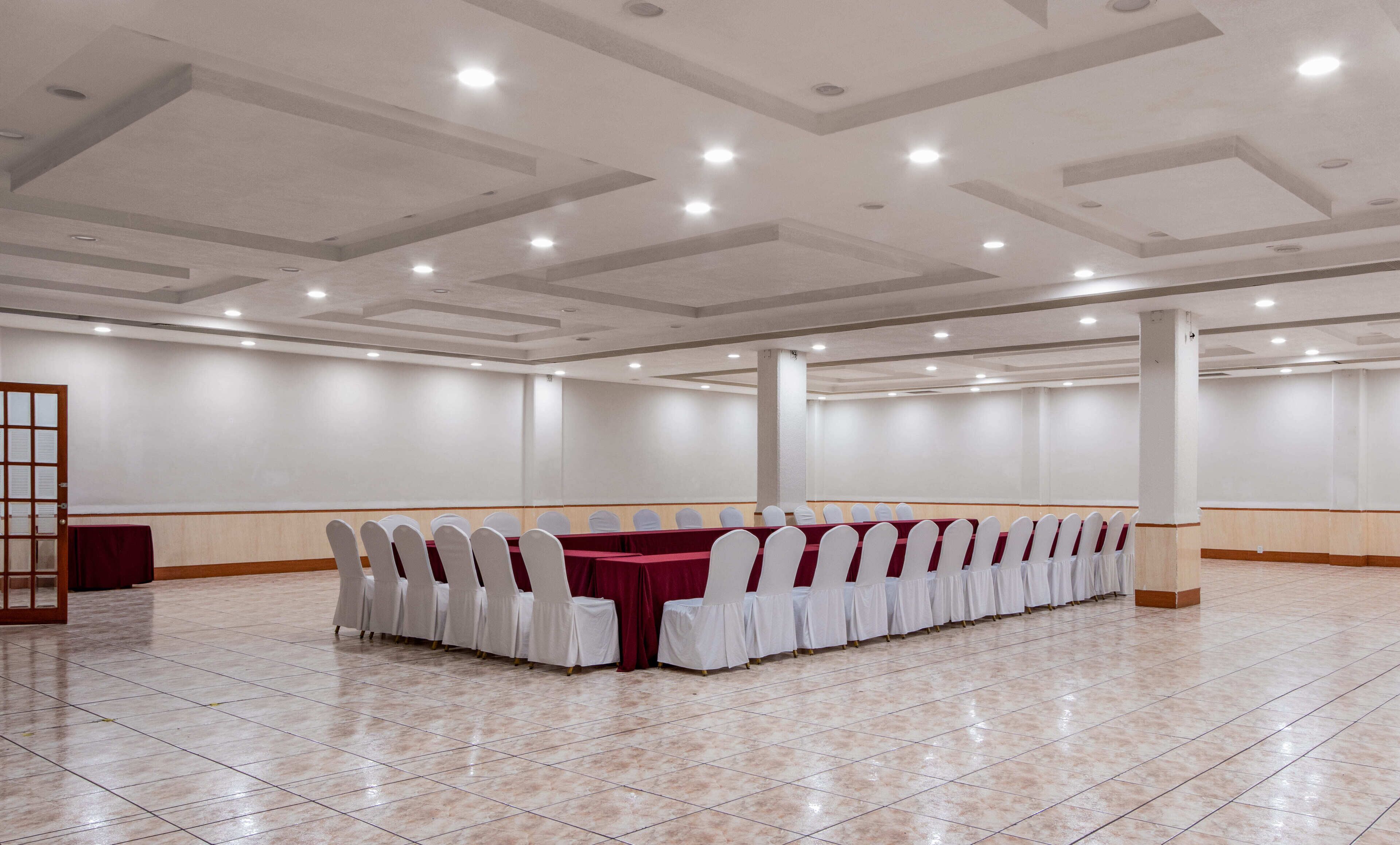 A conference room with a long table, white chairs, and a red tablecloth.