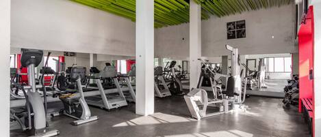 Un gimnasio con varias máquinas de ejercicio, un espejo grande en la pared y techo verde.