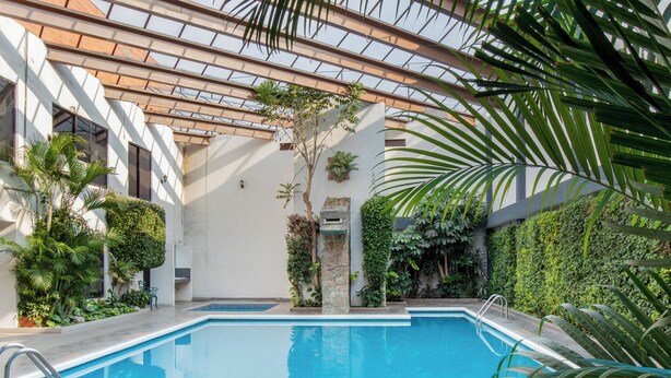 An indoor swimming pool with a glass ceiling, surrounded by greenery and a tiled floor. - Radisson Hotel & Convention Center Toluca (Toluca)