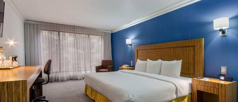 Habitación de hotel con una cama grande, un escritorio con silla, una mesita de noche de madera y una lámpara de pared.