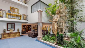 A multi-level hotel lobby with a central atrium featuring a large tree sculpture, a seating area with sofas, and a display of ornate vases. - Radisson Hotel & Convention Center Toluca (Toluca)