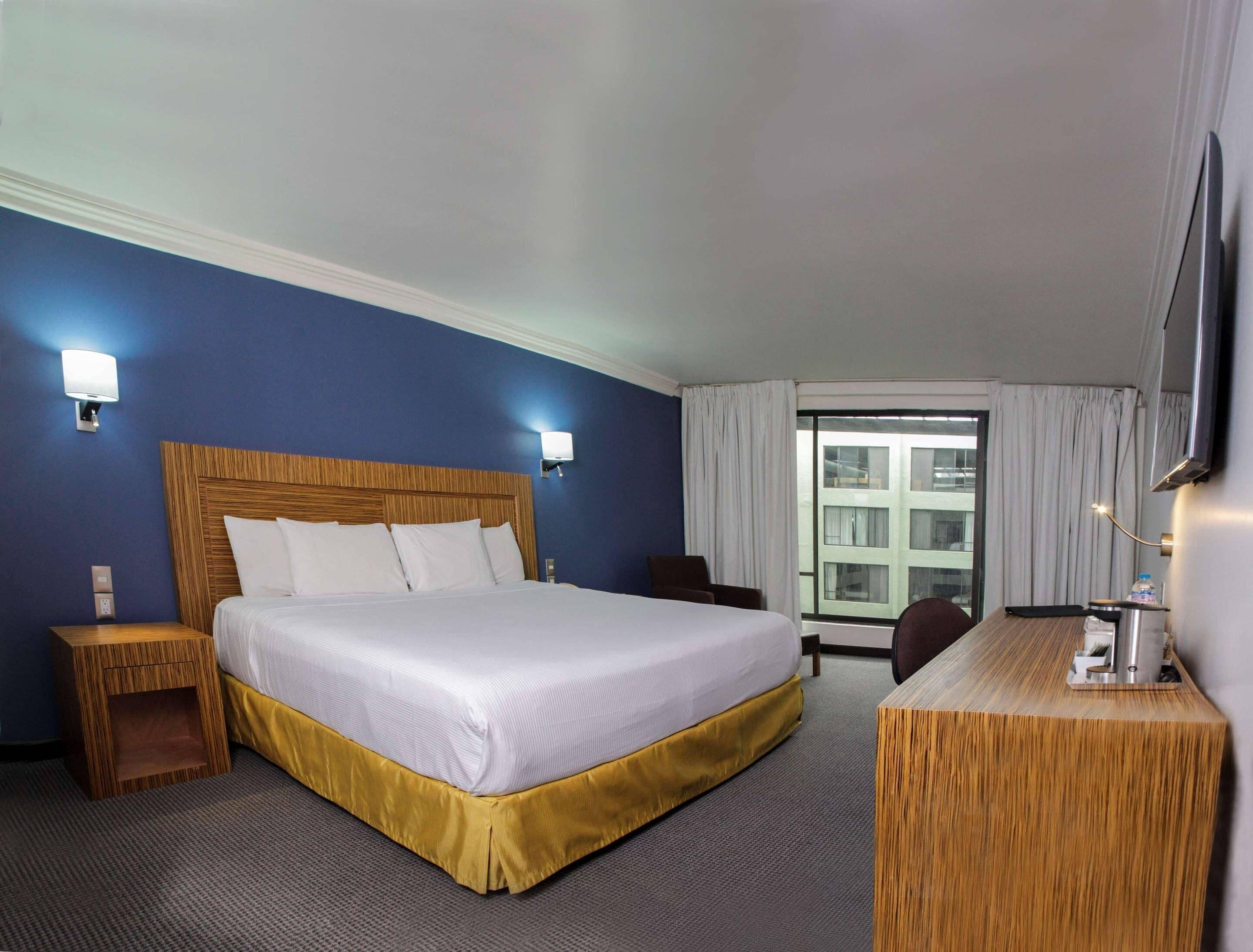 A hotel room with a large bed, bedside tables, a desk, and a TV.