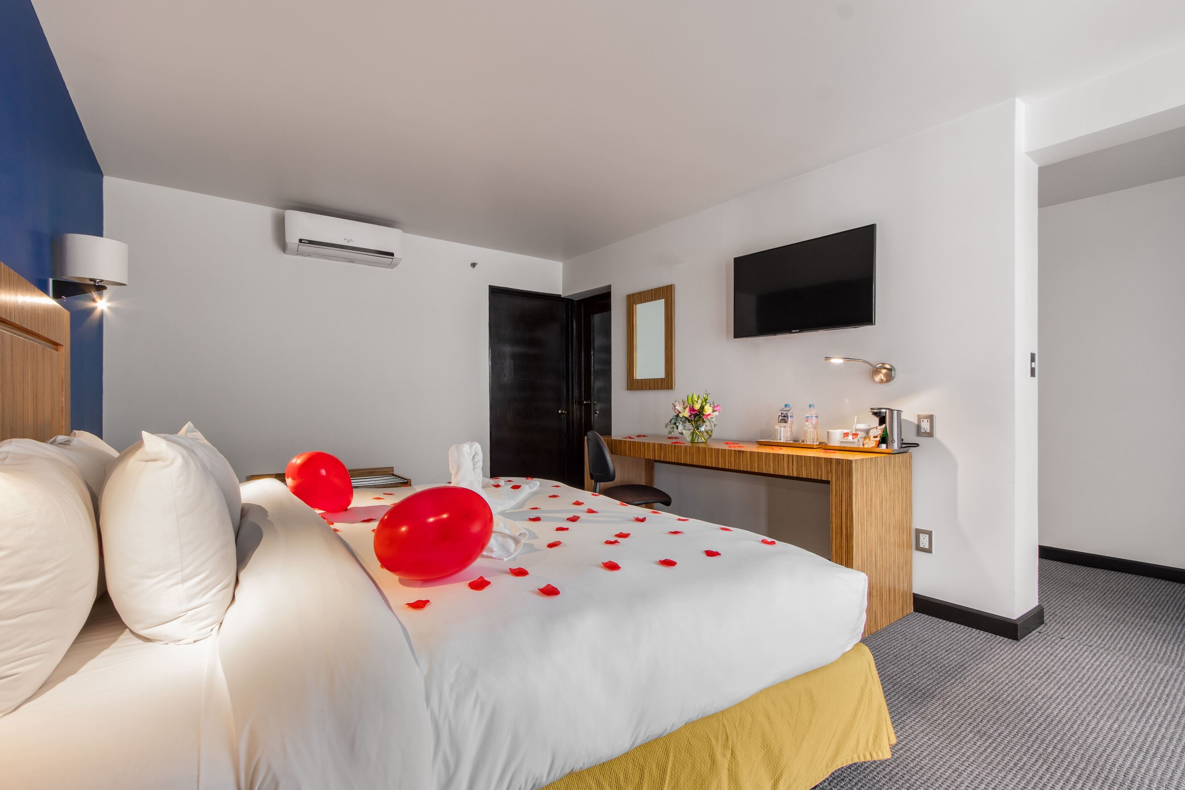 A hotel room with a bed, a desk, a chair, a flat-screen TV, and an air conditioning unit.