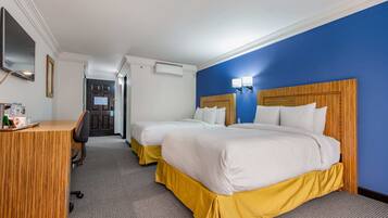 Habitación de hotel con dos camas, un escritorio, un espejo y una puerta que da a un pasillo.