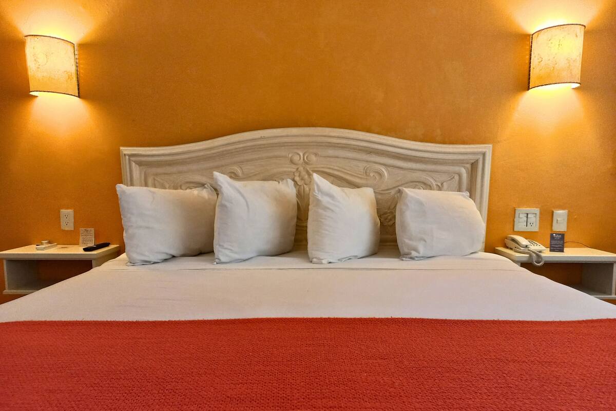 A hotel room with a large bed, white bedding, and a red throw blanket. There are two bedside tables with lamps and a phone.