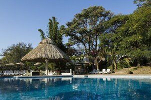 Una piscina con sillas de descanso y una estructura de techo de paja.