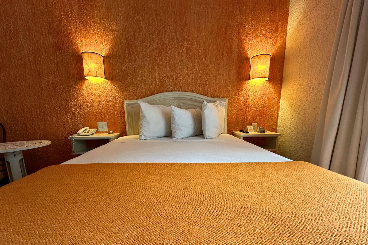A hotel room with a large bed, two bedside tables, a telephone, and wall-mounted lamps.