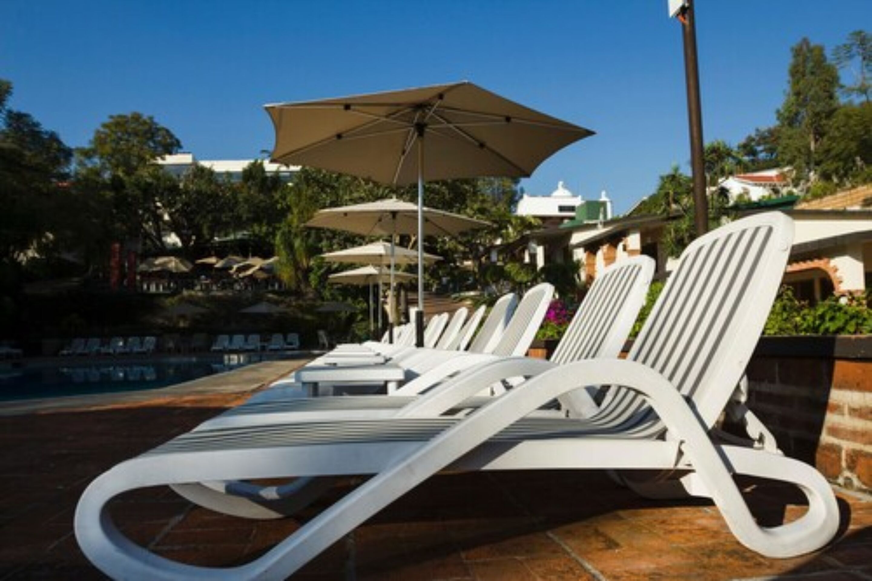 Un área junto a la piscina con sillas de descanso blancas y sombrillas.