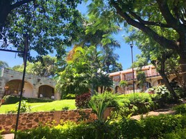 Un patio con muro de piedra, abundante follaje y un edificio con puertas arqueadas.