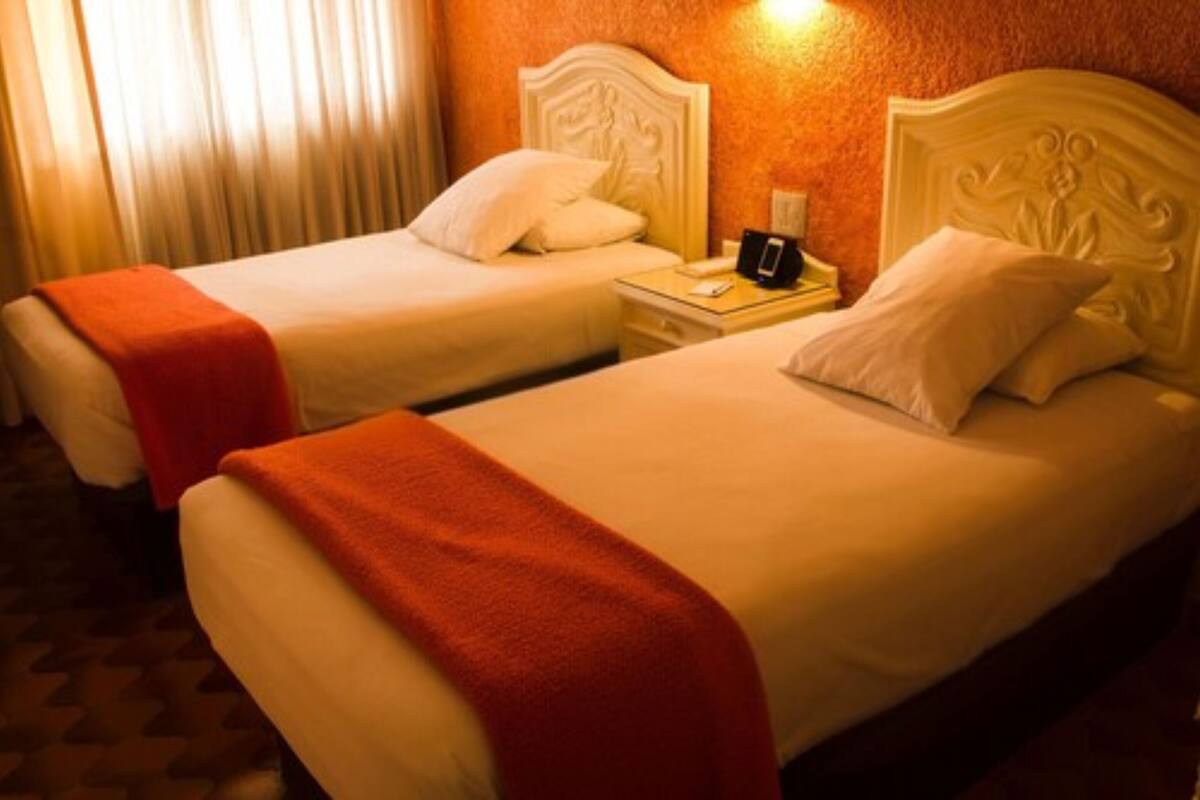 Two beds with white headboards and red blankets, a bedside table with a phone, and a curtain in the background.