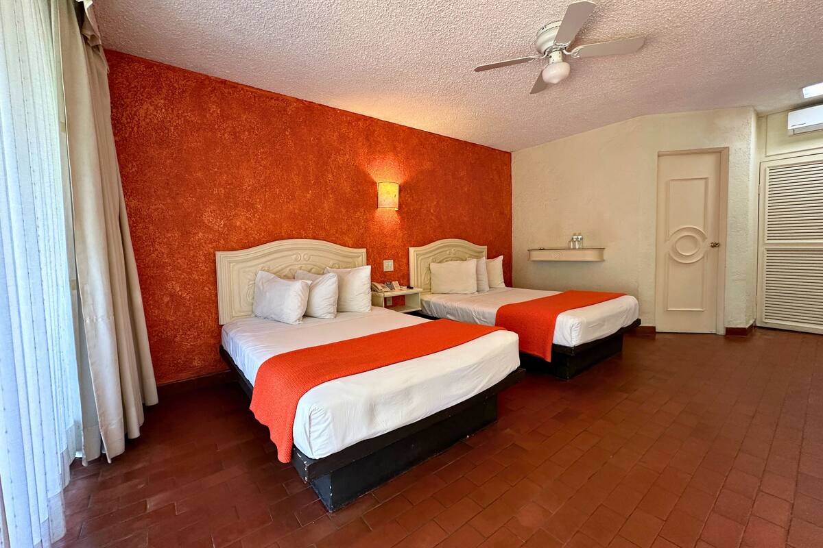 A hotel room with two beds, a ceiling fan, and a door.