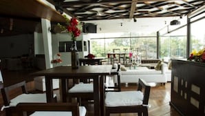 Un comedor con mesas y sillas de madera, un sofá blanco y un amplio ventanal con vistas al exterior.