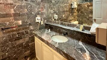Un baño con lavamanos de mármol, un espejo grande y un perchero para toallas.