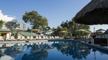 Una piscina con tumbonas y sombrillas, rodeada de edificios y árboles.