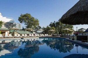 Una piscina con tumbonas y sombrillas, rodeada de edificios y árboles.