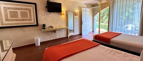A hotel room with two beds, a ceiling fan, a mounted TV, a small shelf with items, and a view of the outdoors.