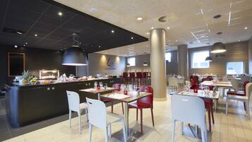Un restaurant modern amb una zona de bar central, diverses taules de dinar amb caires i una cuina al fons.