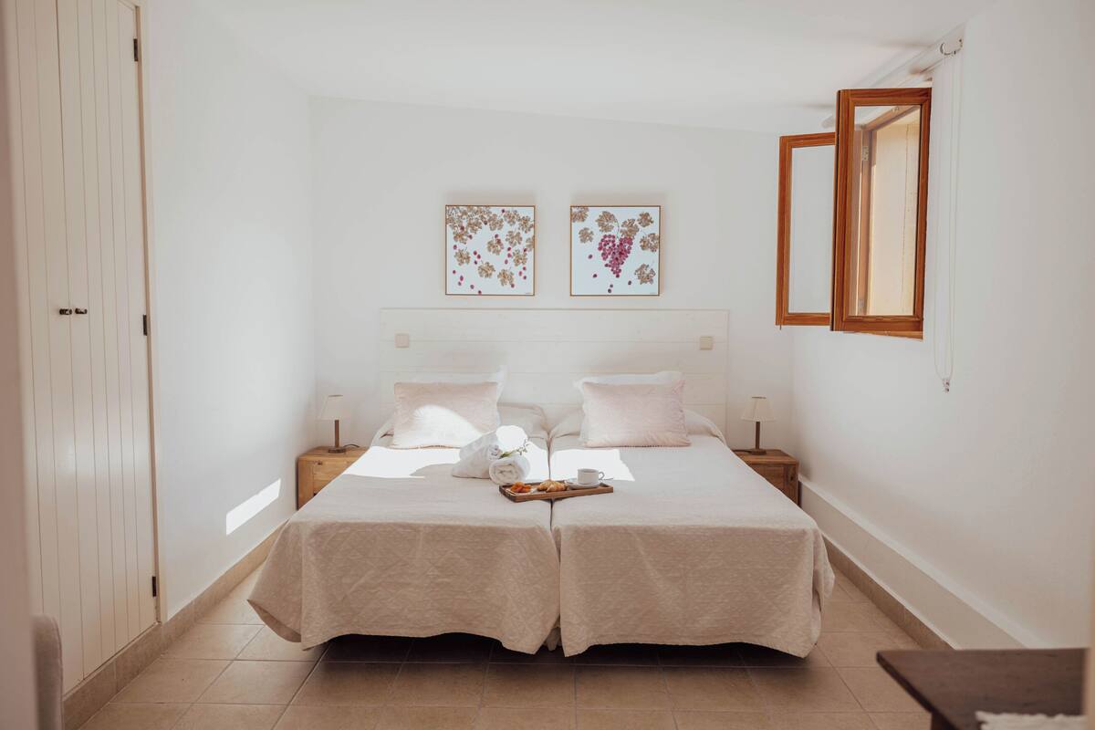 A double bed with a tray of breakfast items, two bedside tables, and two framed artworks on the wall.