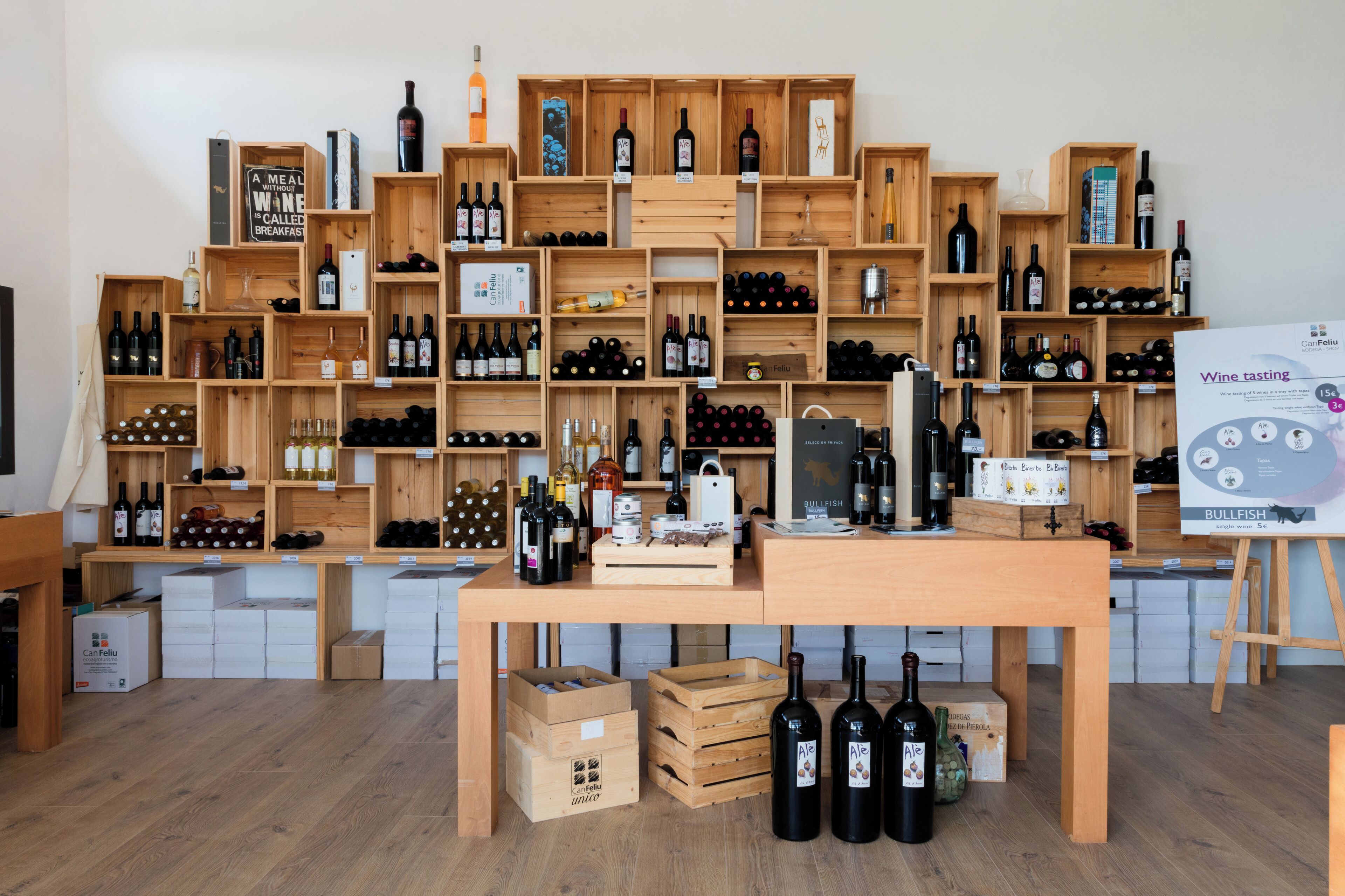 Una sala de degustación de vinos con estantes de madera que exhiben varias botellas y una mesa con más botellas y un cartel sobre la degustación.