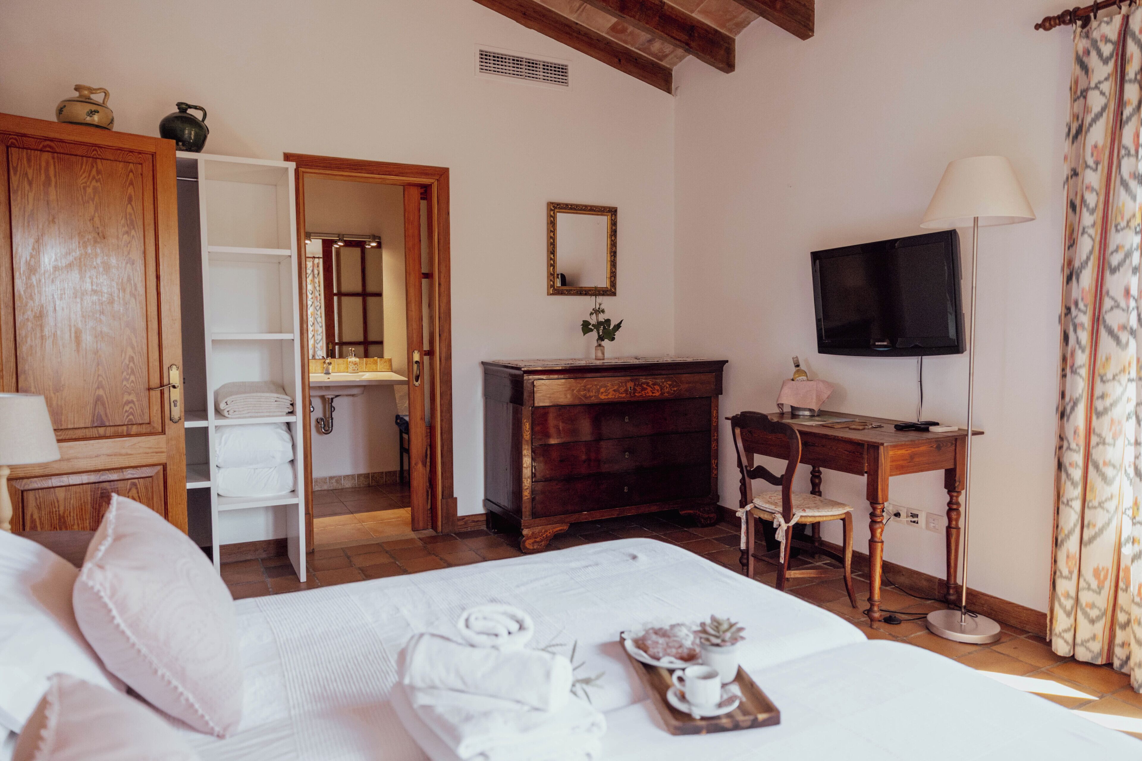 Habitación de hotel con cama, cómoda de madera, escritorio con silla, televisor y baño visible a través de una puerta abierta.
