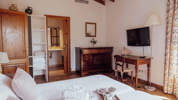 Habitación de hotel con cama, cómoda de madera, escritorio con silla, televisor y baño visible a través de una puerta abierta.
