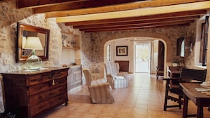 A stone-walled room with a wooden ceiling, a dresser, two armchairs, a table, and a mirror. - Hotel Rural Can Feliu (Porreres)