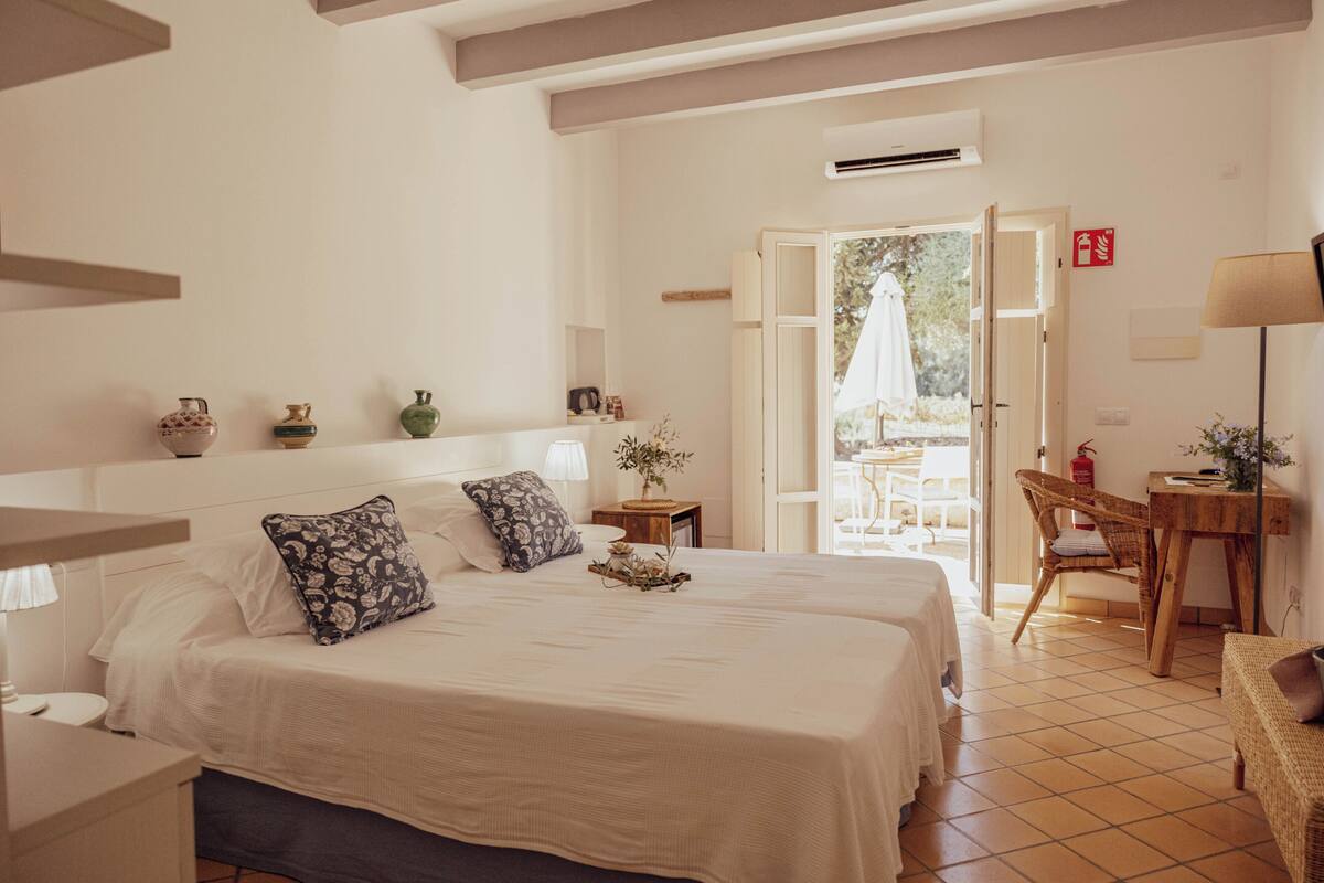 A hotel room with two beds, a desk, a chair, and a view of the outside.