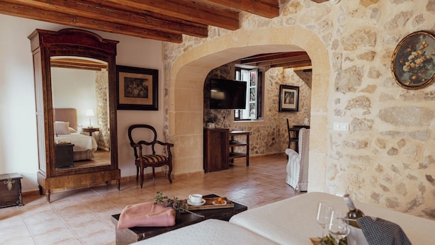 A room with a bed, a wooden dresser, a television, and a stone wall. - Hotel Rural Can Feliu (Porreres)