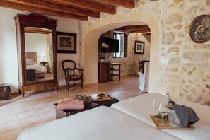 A room with a bed, a wooden dresser, a television, and a stone wall.