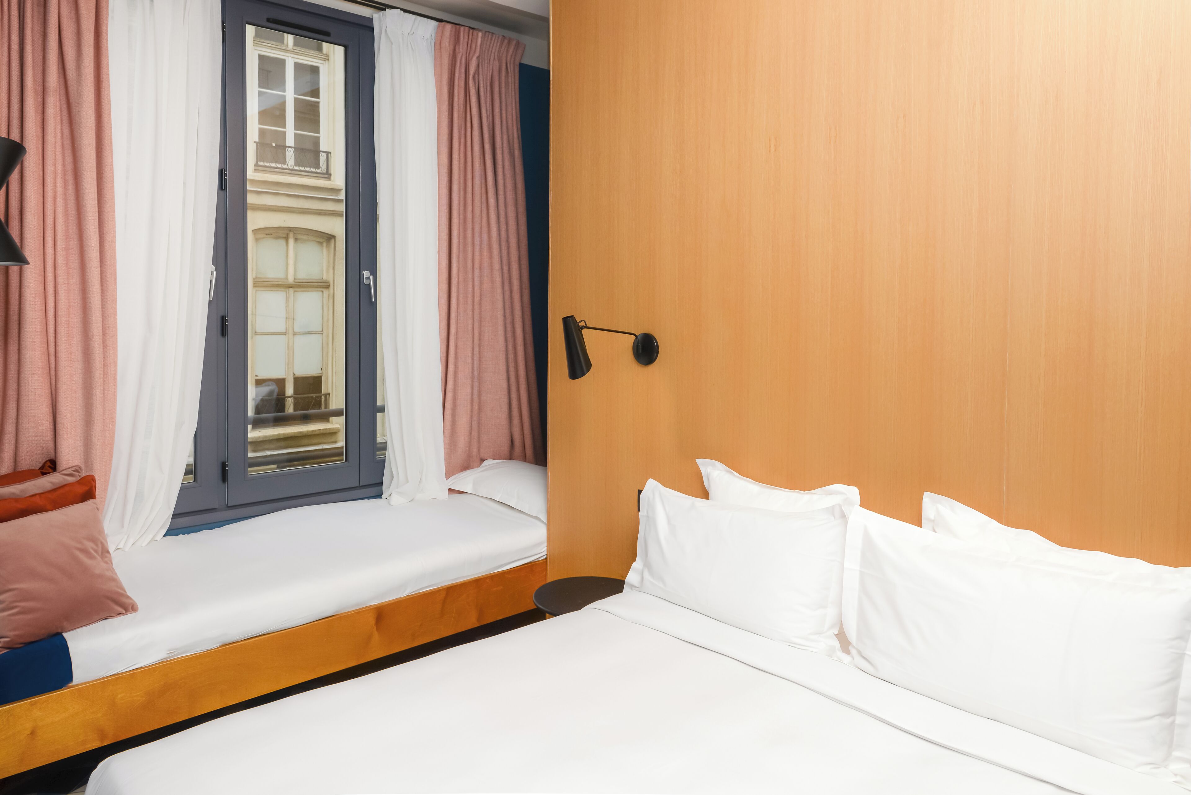 A hotel room with a bed, a window with curtains, a bedside table, and a lamp.