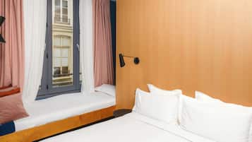 A hotel room with a bed, a window with curtains, a bedside table, and a lamp.