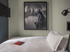 Une chambre d’hôtel avec un lit, une photographie encadrée accrochée au mur, une lampe de chevet et un livre posé sur le lit.