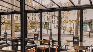 A café with round tables and chairs, a glass storefront, and a view of the street outside. - Hôtel Edgar & Achille (Paris)