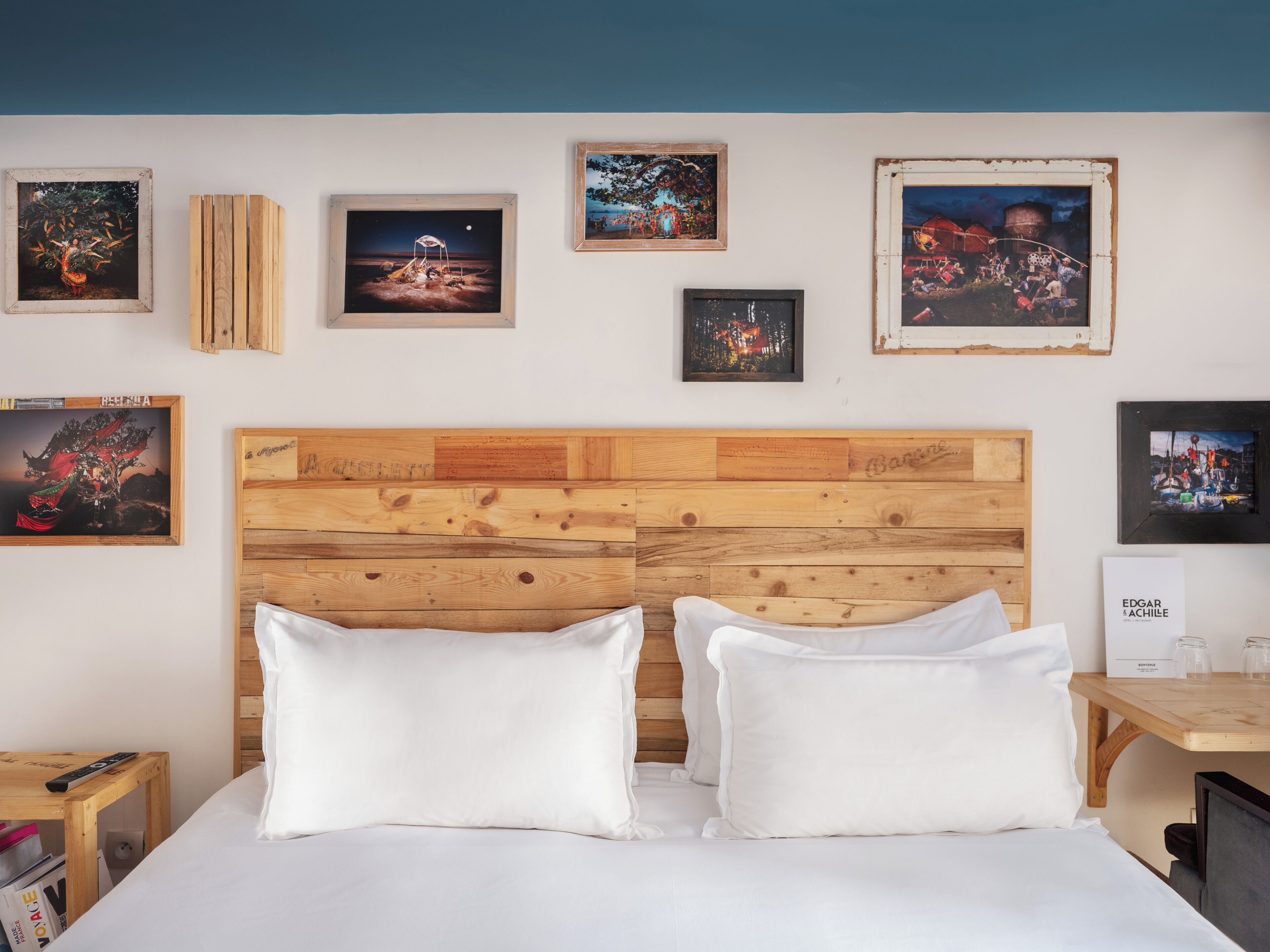 A hotel room with a wooden headboard, white bedding, and several framed artworks on the wall.