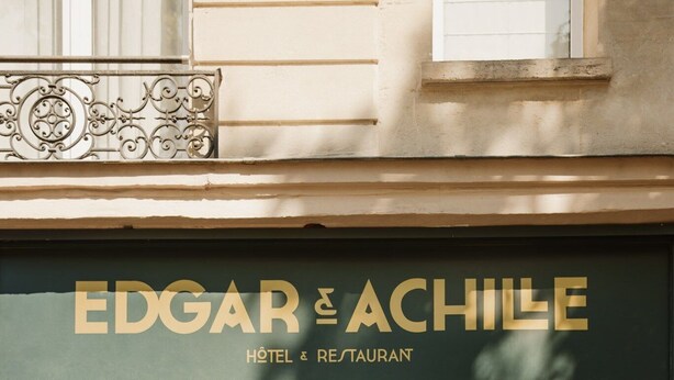 La entrada del hotel Edgar & Achille, con un cartel sobre la puerta y un cartel a la derecha.