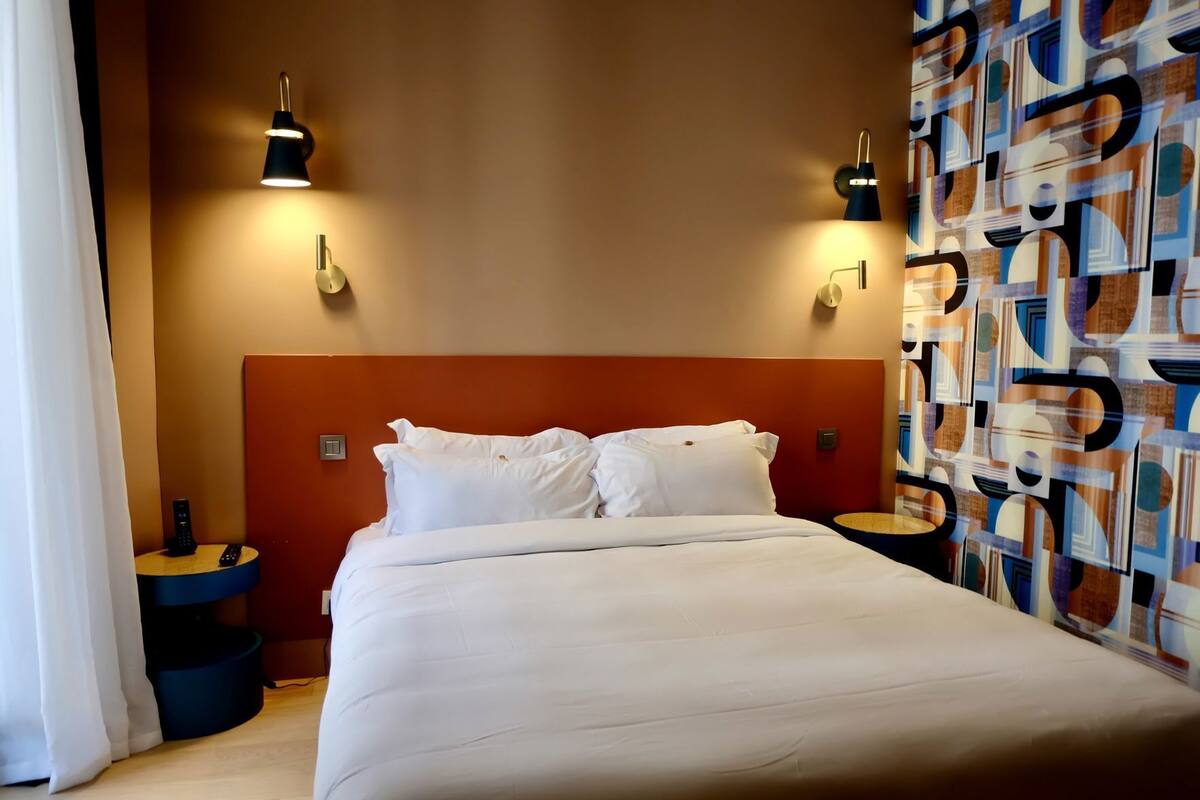 A hotel room with a large bed, two bedside tables, and two wall-mounted lamps.