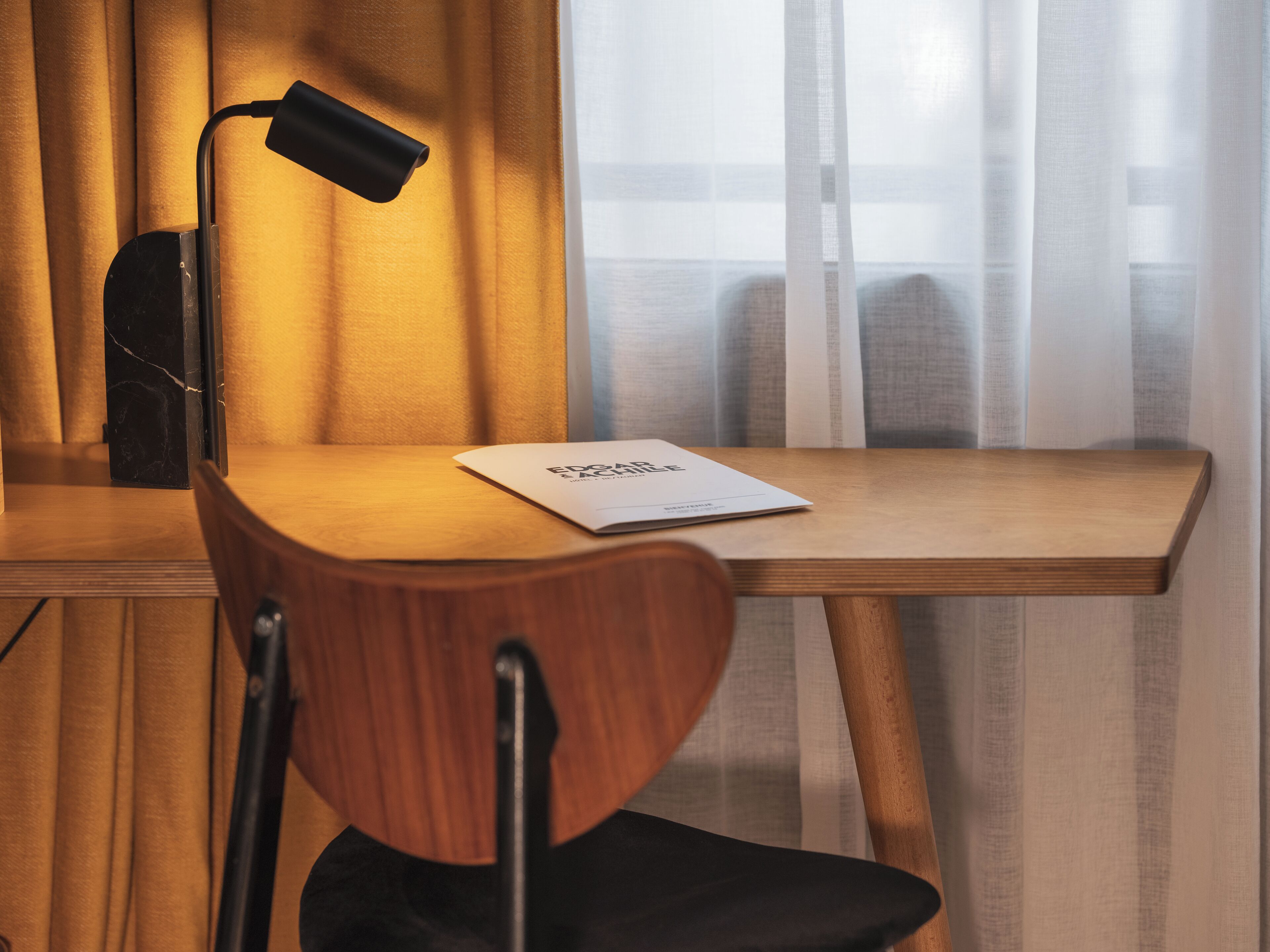 Een houten bureau met een zwarte lamp, een stoel en een boekje op het bureau.