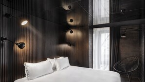 Un dormitorio moderno con una cama grande, varias luces fijadas a la pared y una silla.
