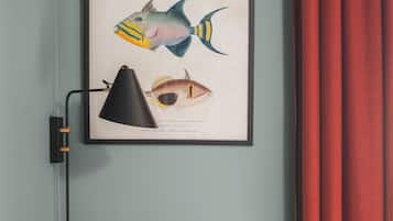 A framed fish illustration on a wall, a desk with a chair, a lamp, and two glasses on the desk.